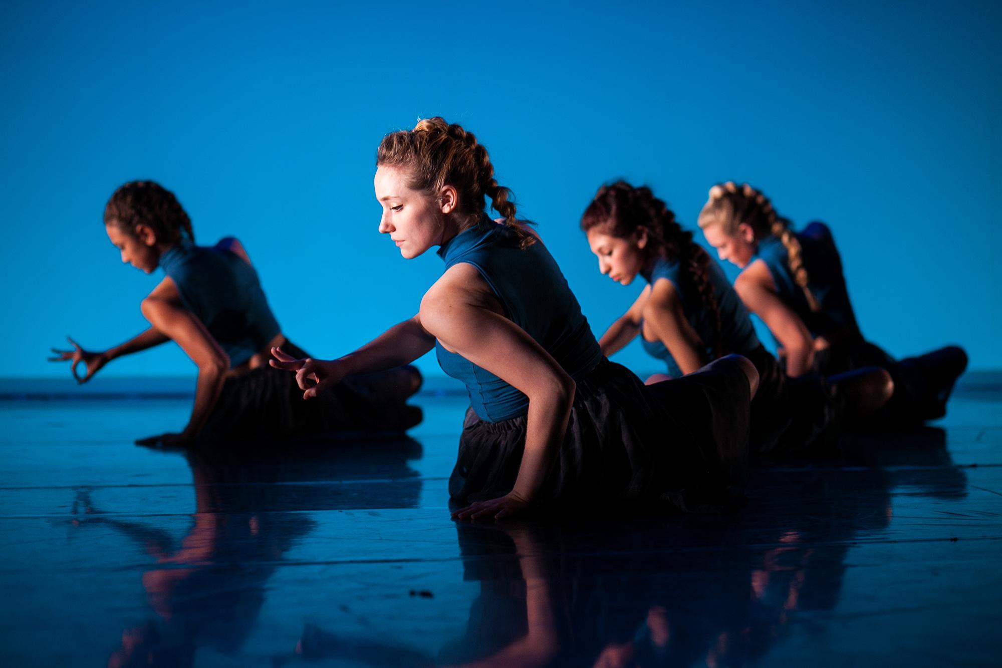 four dancers on the ground against a blue backdrop