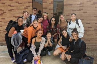 13 UT dance students smile together in front of a brick wall at the ACDA regional conference