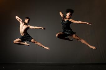 Two dancers caught mid-jump with their left legs and arms extended and their right arms and legs bent