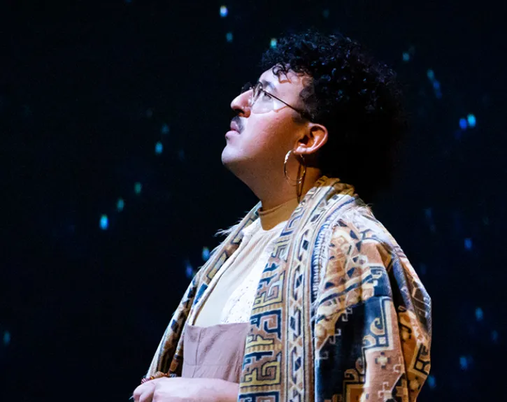 A graduate student performs in a production, with a starry night sky projected behind them