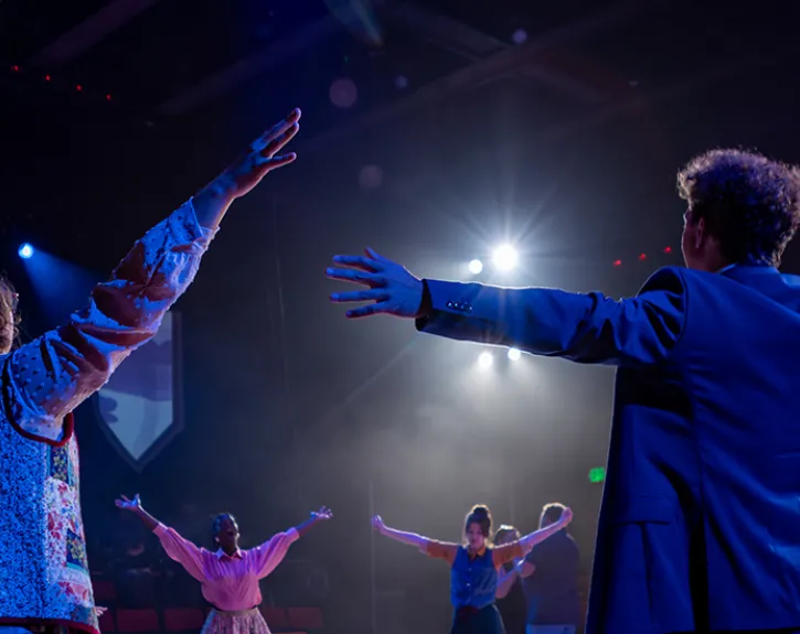 Undergraduate performers stand in a circle and stretch before a tech rehearsal