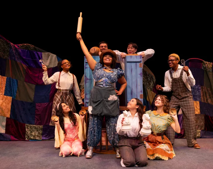 A girl in a blue dress upholds a rolling pin