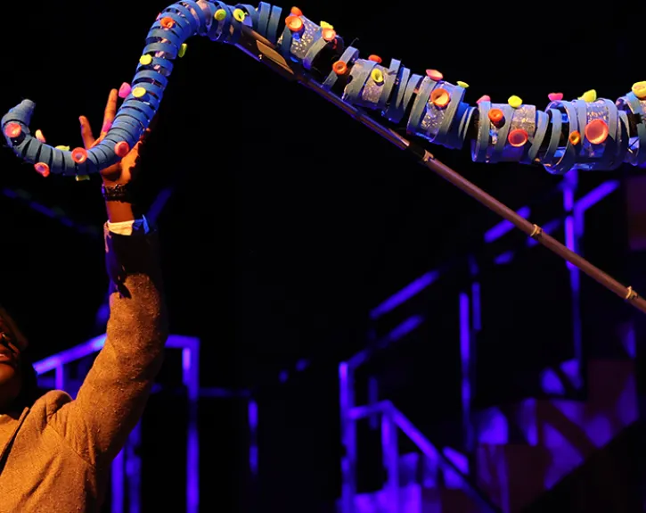 An actor performing in JAMES AND THE GIANT PEACH looks with curiosity at a glowing paper bag