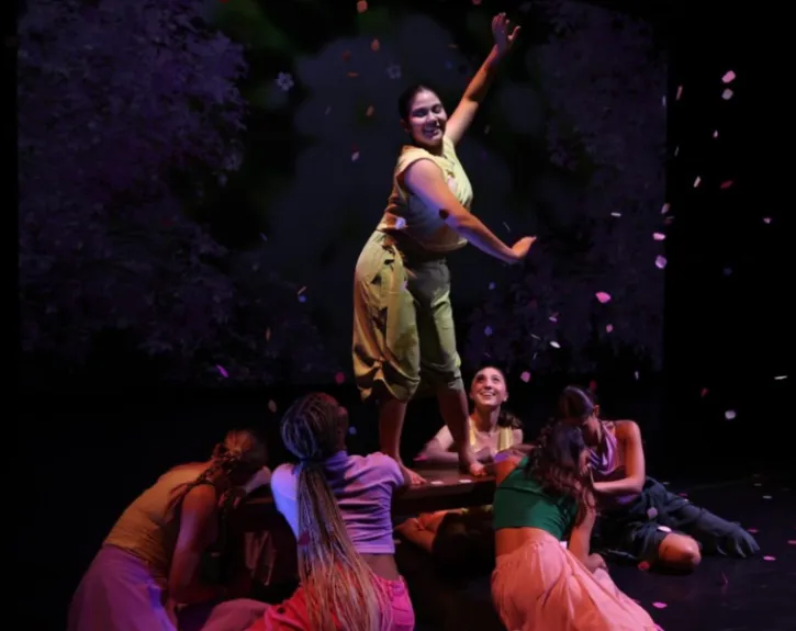 A woman wearing a green costume extends her arms