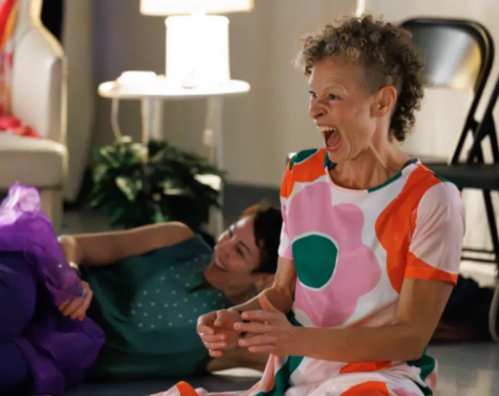 A woman with curly hair wearing a colorful shirt laughs