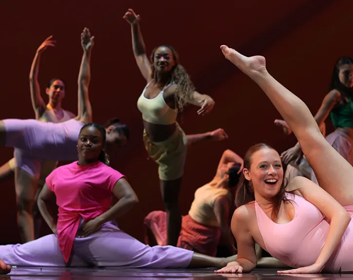 A large group of dancers pose in a final, joyful dance move at the end of a dance piece
