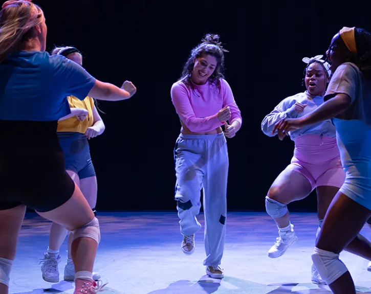 A group of students dance joyfully in a circle on stage