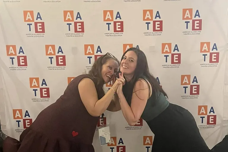 Roxanne Schroeder-Arce and Cay Schaefer pose together in front of a large backdrop for AATE