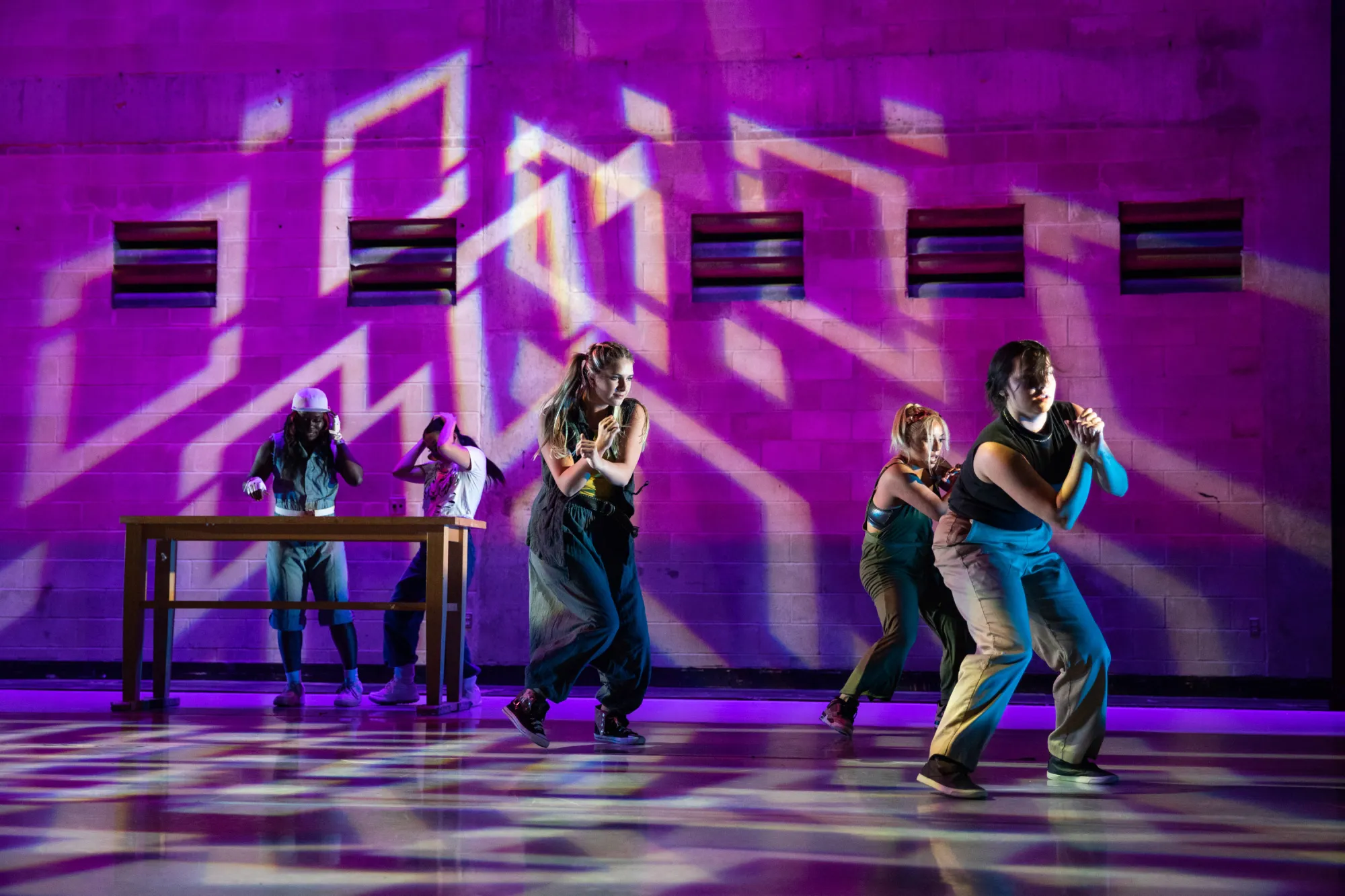 five dancers on stage with purple, geometric stage lighting