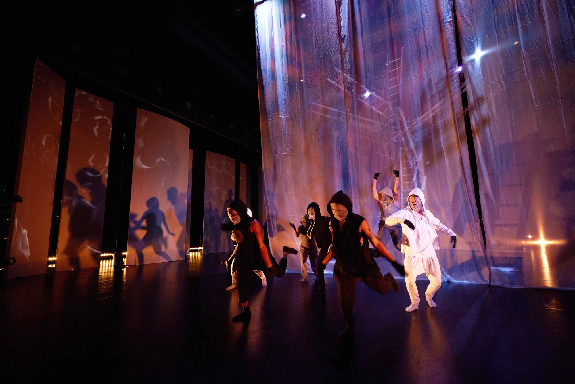 dance ensemble dressed in all black and white moving, with their shadows cast on the wall next to them