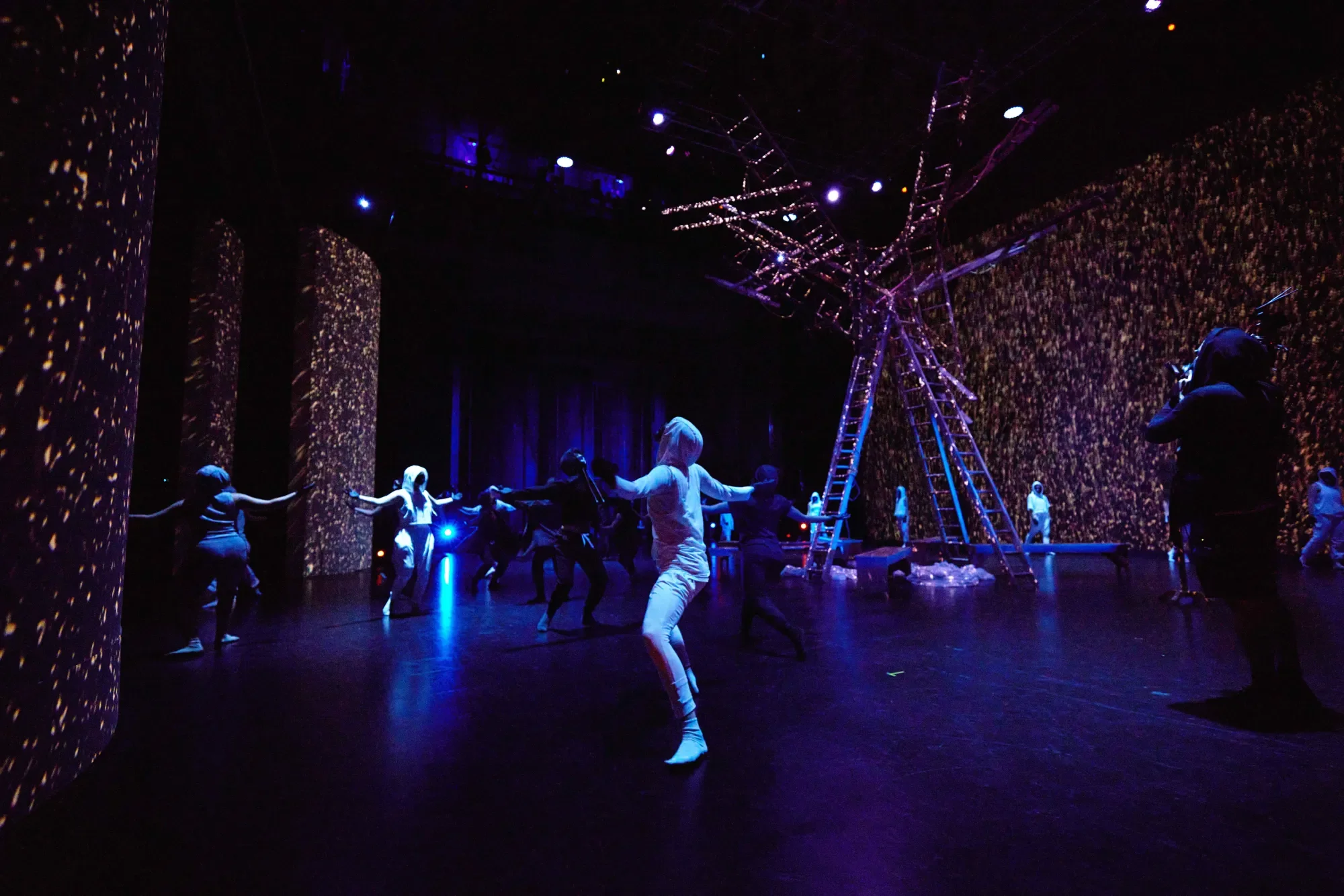 an ensemble of dancers move with their arms outstretched, washed in white, rain-like projections