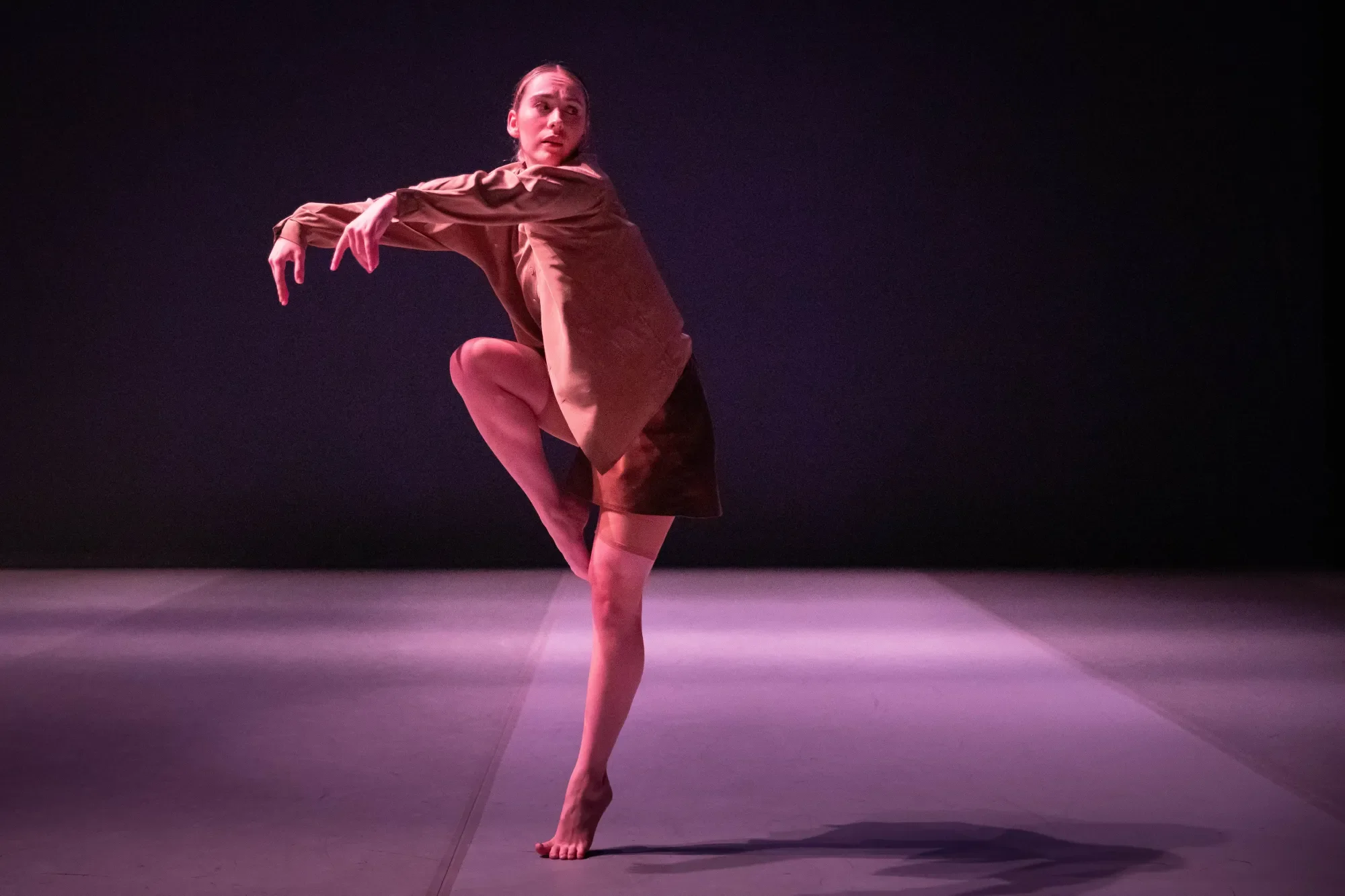 dancer wearing shades of brown and tan balances on her left foot, with her right knee and arms lifted