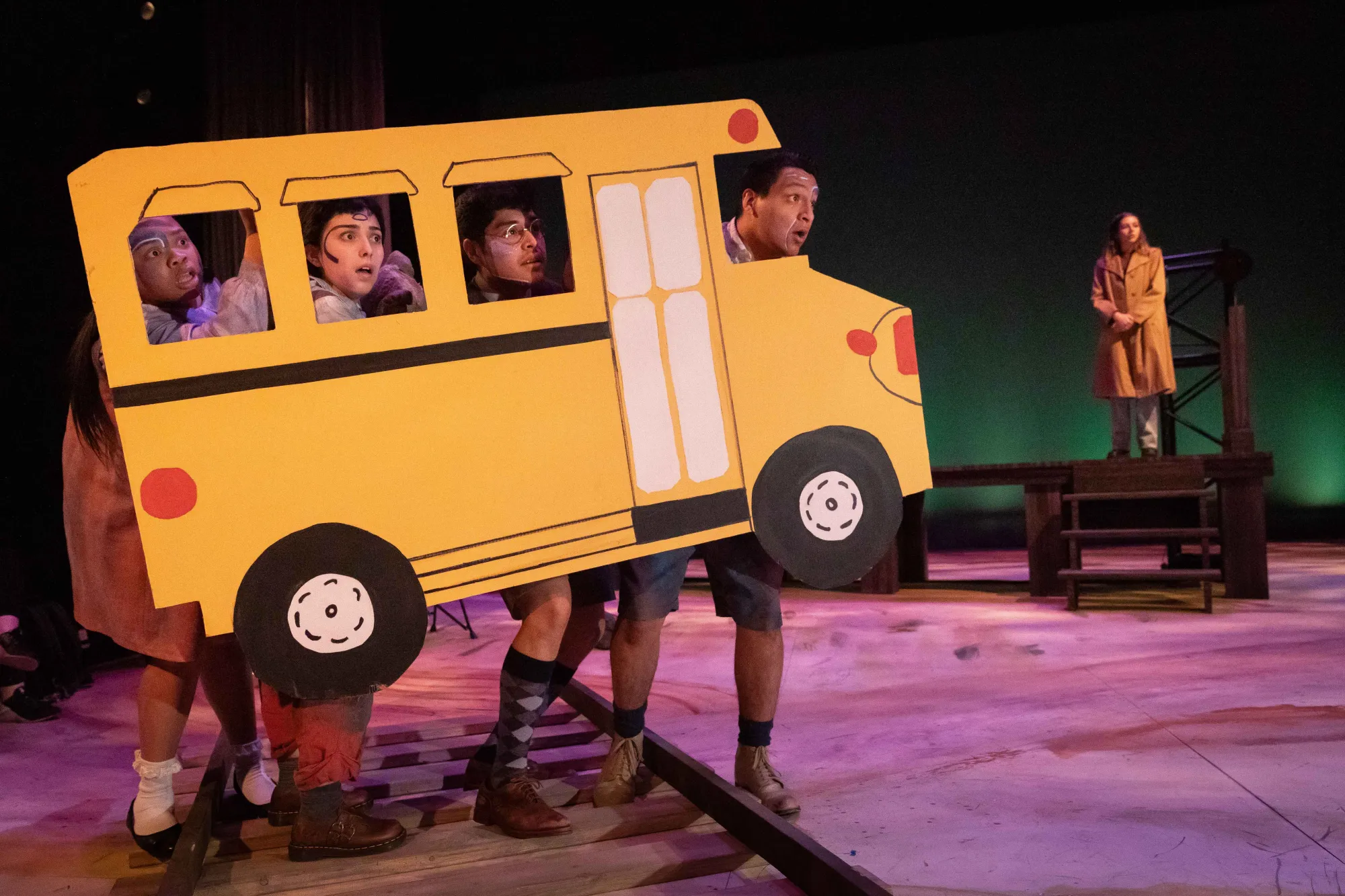 four "Ghost Children" stand on train tracks behind a bus made of paper, looking concerned