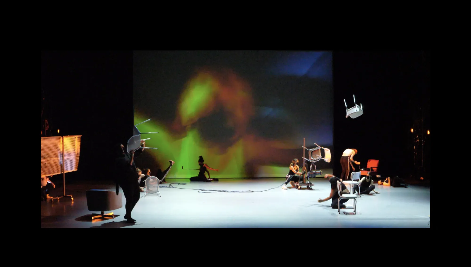 dancers move on stage, with chairs placed in different ways and hanging around them