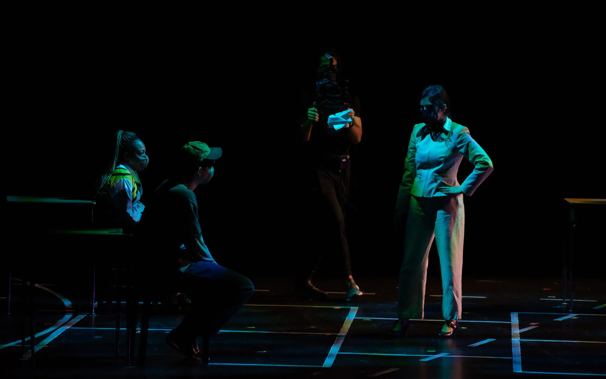 actors wearing masks stand on stage, washed in blue light