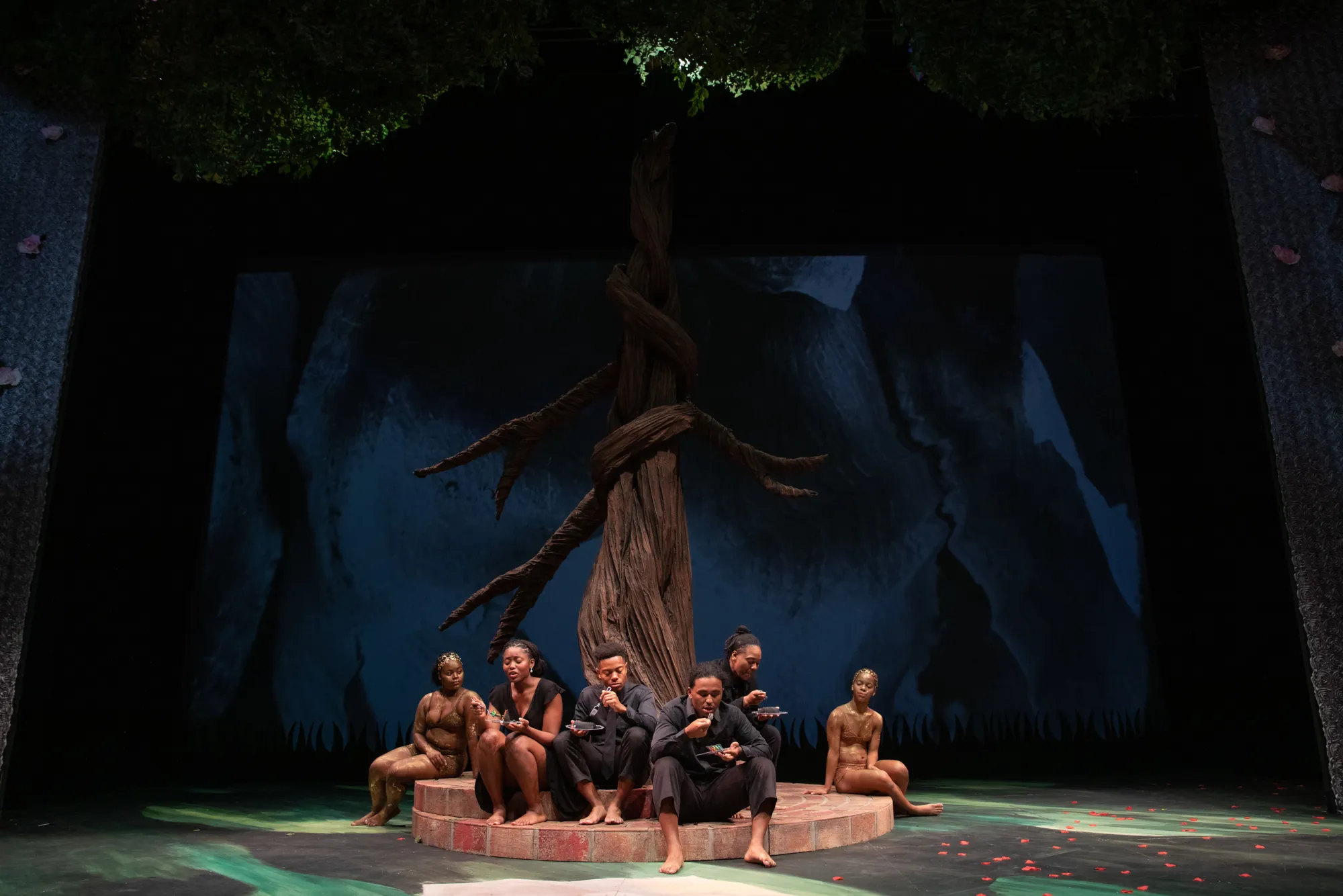 People wearing gold and black lounge under a giant tree