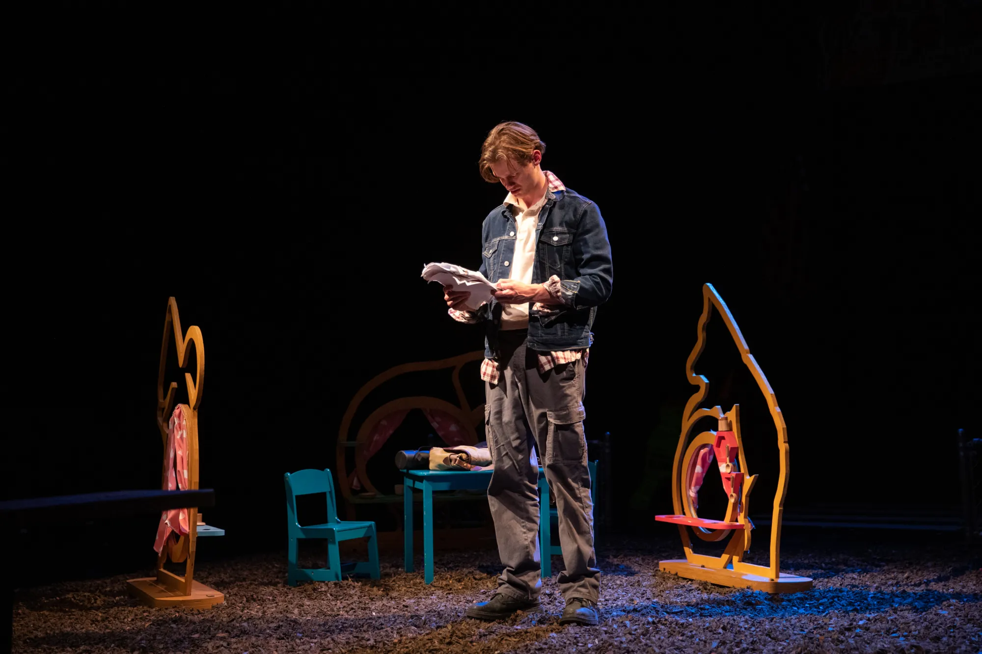 Actor Oliver Aaro as Arthur stands surrounded by the magical playground equipment he built looking at a flyer for armored backpacks.