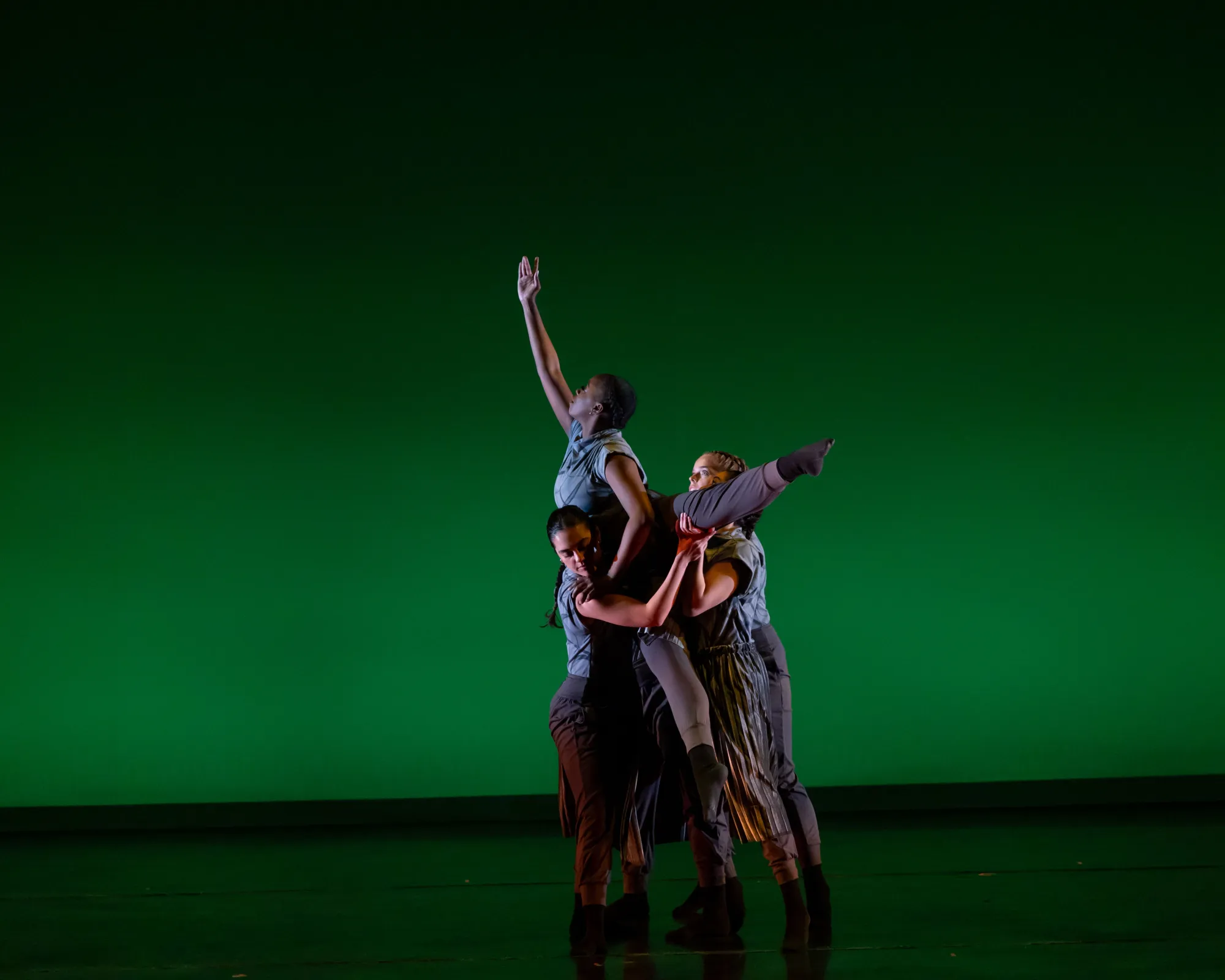 3 dancers of Points of Intersection hold a forth dancer in a lift, where the lifted dancer reaches toward the sky with a leg and foot extended to the side.