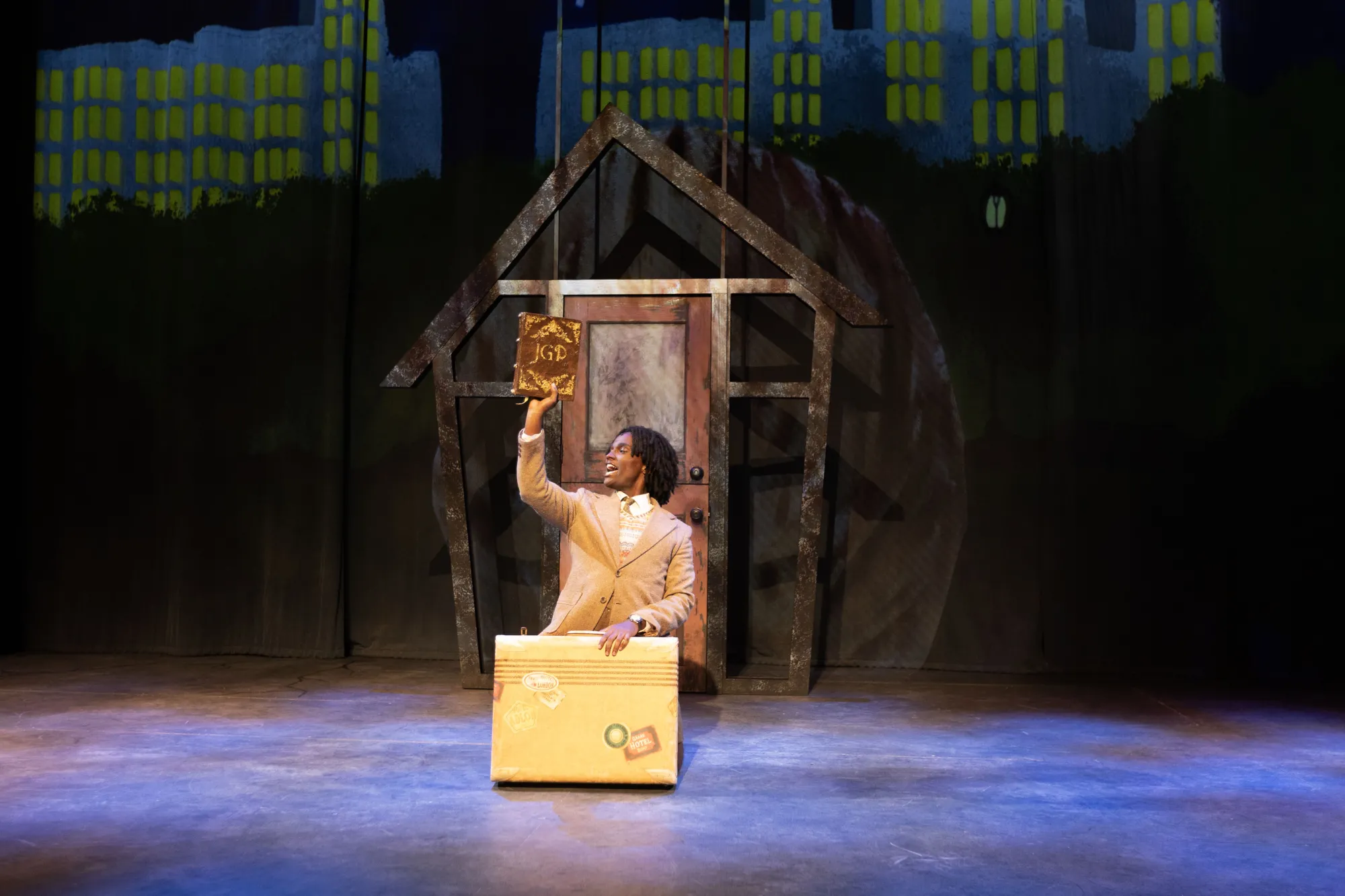 James, played by Trevor Gatabaki, lifts up triumphantly the book James and the Giant Peach. Quick, gather round - he is about to tell his story!