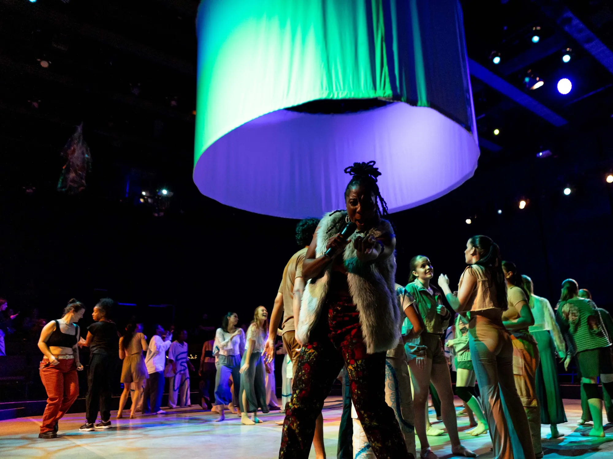 MC, Aysha Upchurch, points at the camera while dancers move behind her.