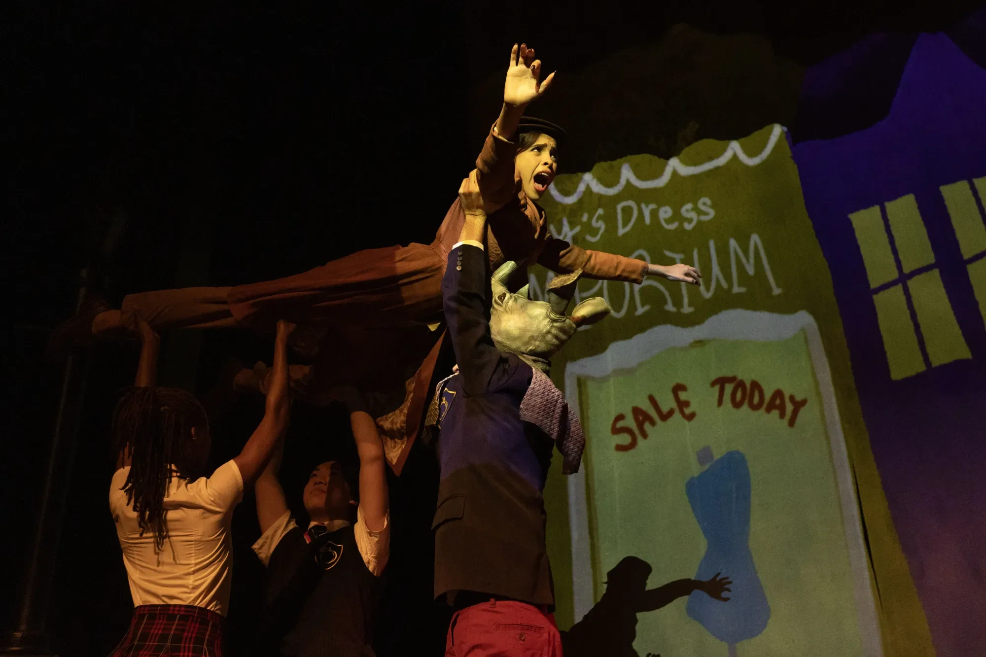 In a feat of physical brillance, student 4, played by Belen Tamez, soars above the heads of the other students. She is, of course, being held above their heads by their hands.