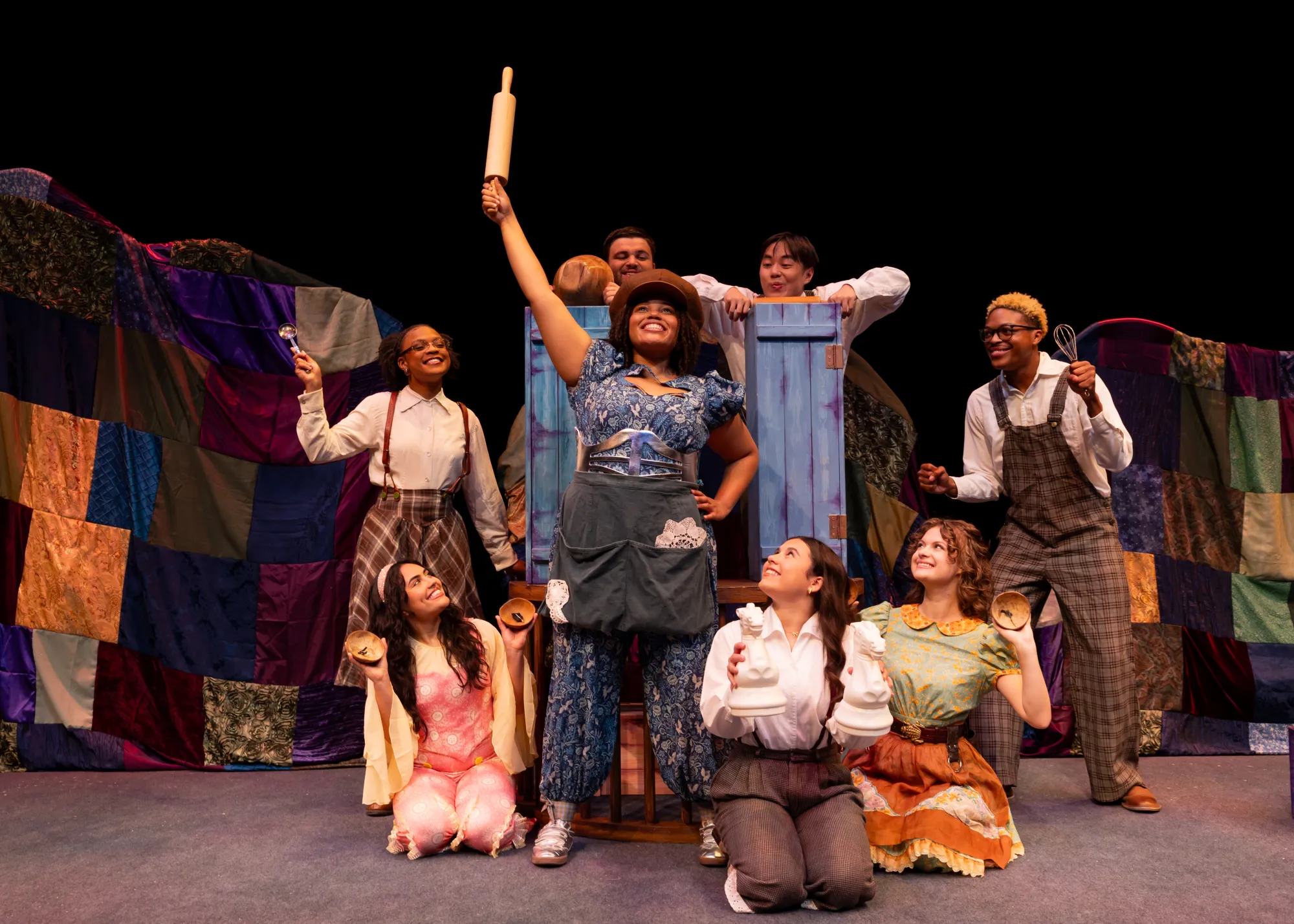 A girl in a blue dress upholds a rolling pin