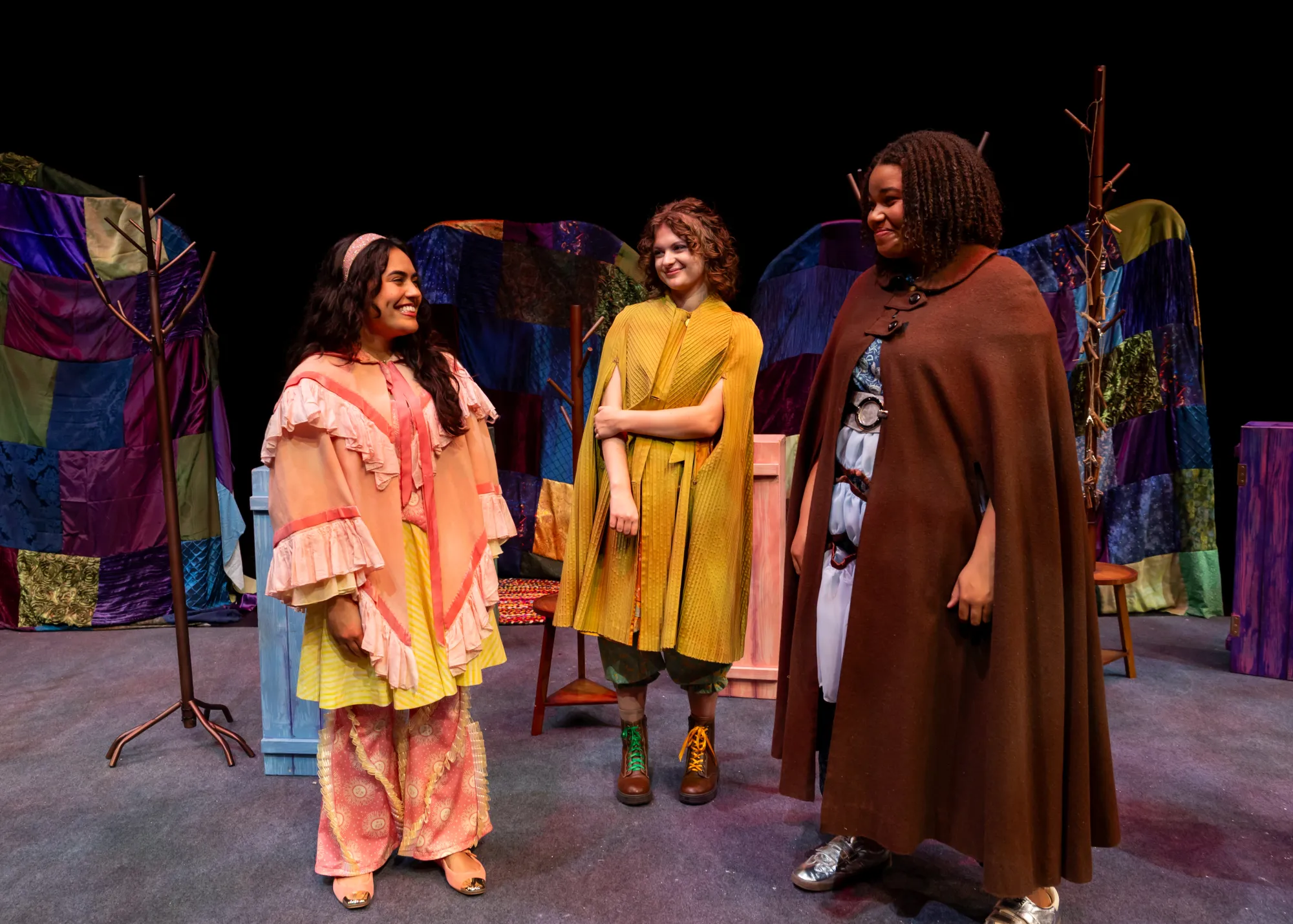Three girls stand in cloaks