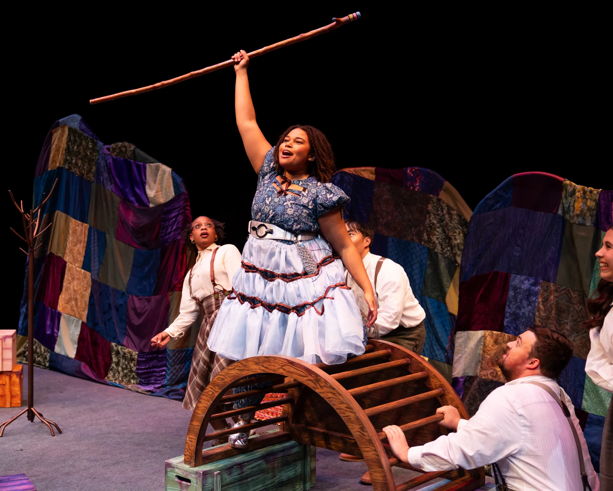 A girl in a blue dress extends a staff into the air