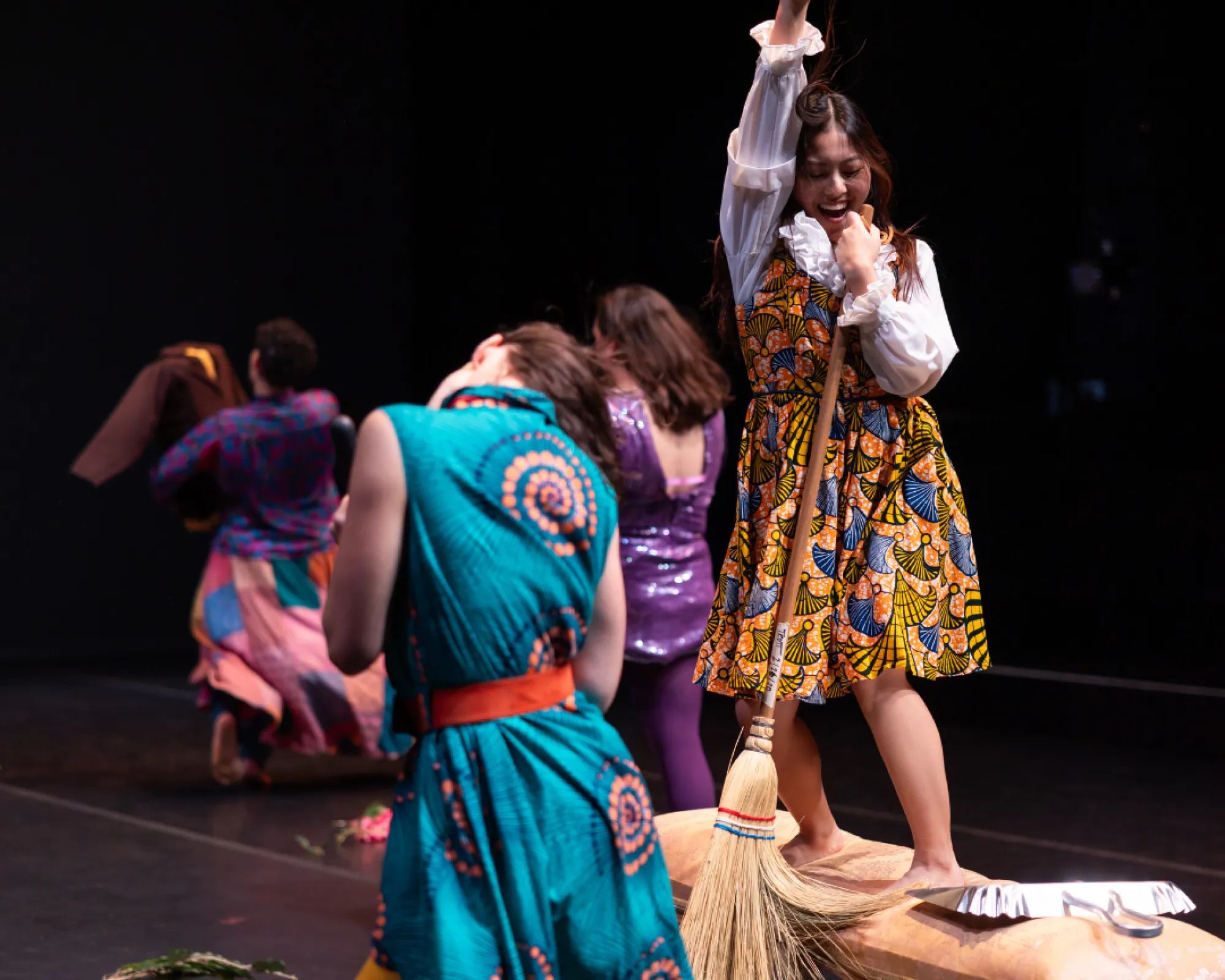 A woman holds a broom and lip-syncs