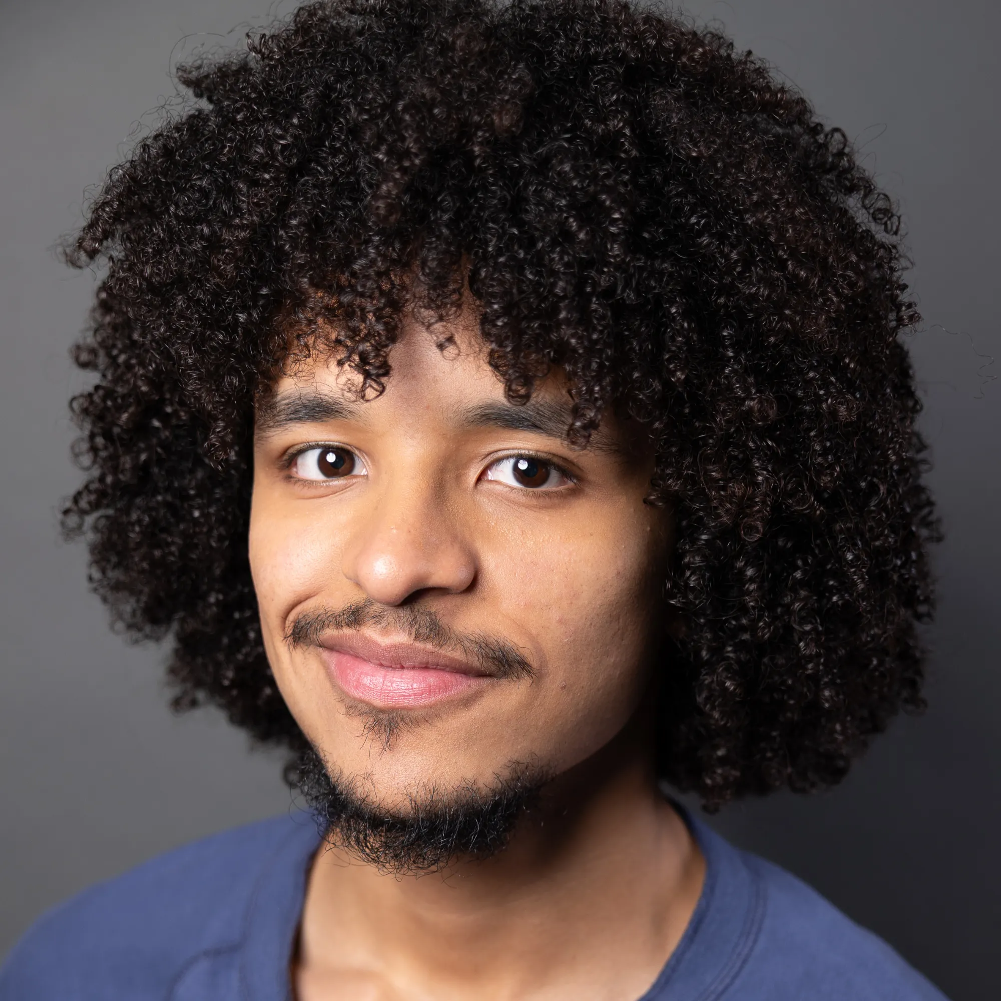 A man with dark curly hair and a beard smiles