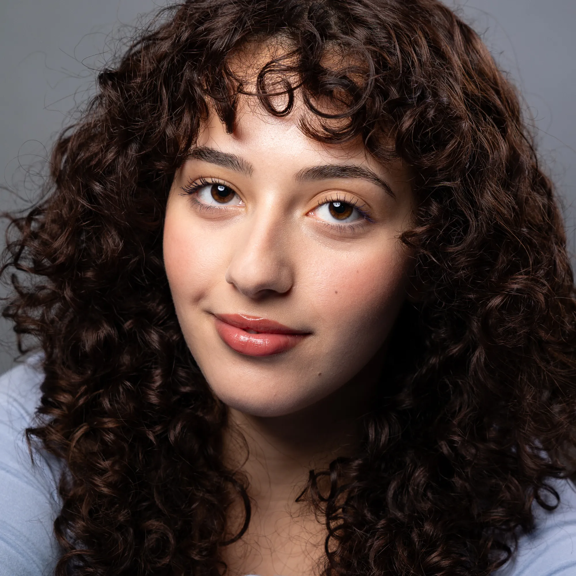 A woman with long brown curly hair smiles