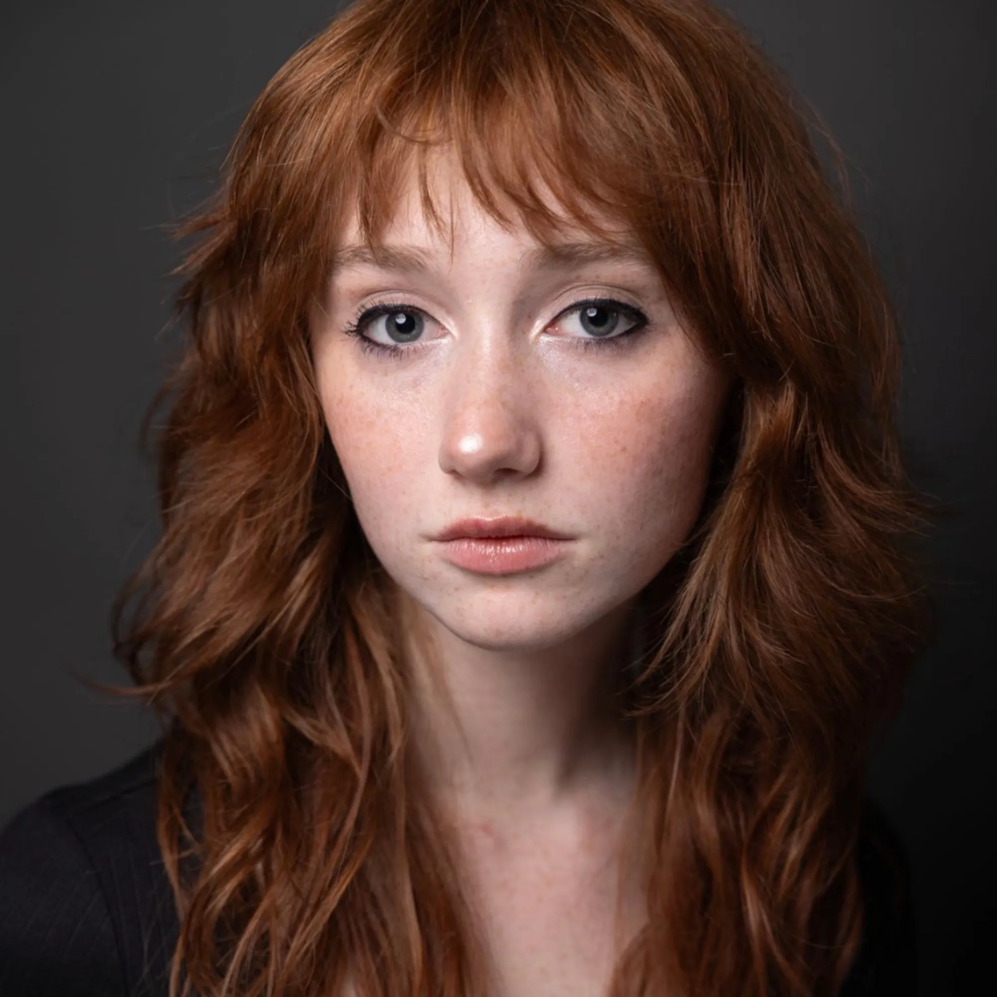 A woman with long red hair turns toward the camera
