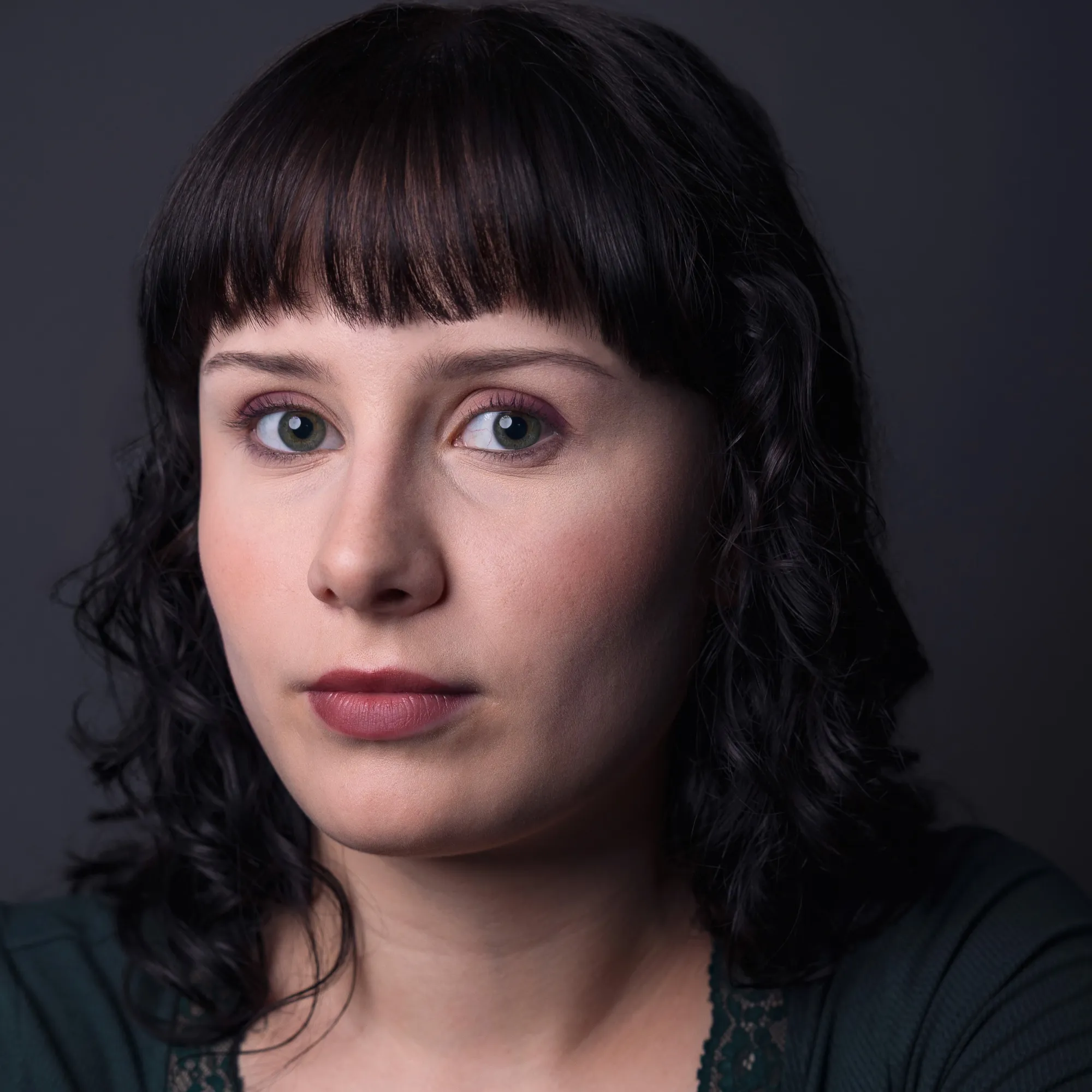 A woman with short hair and bangs looks towards the camera