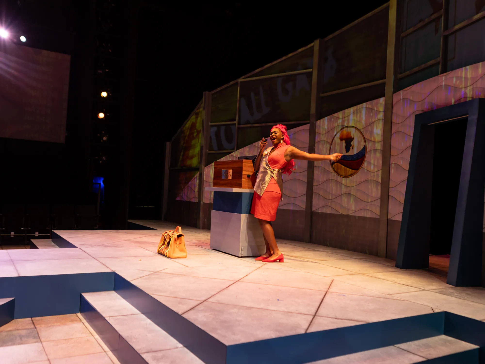 An actor in a red dress with long red hair cheers into an intercom