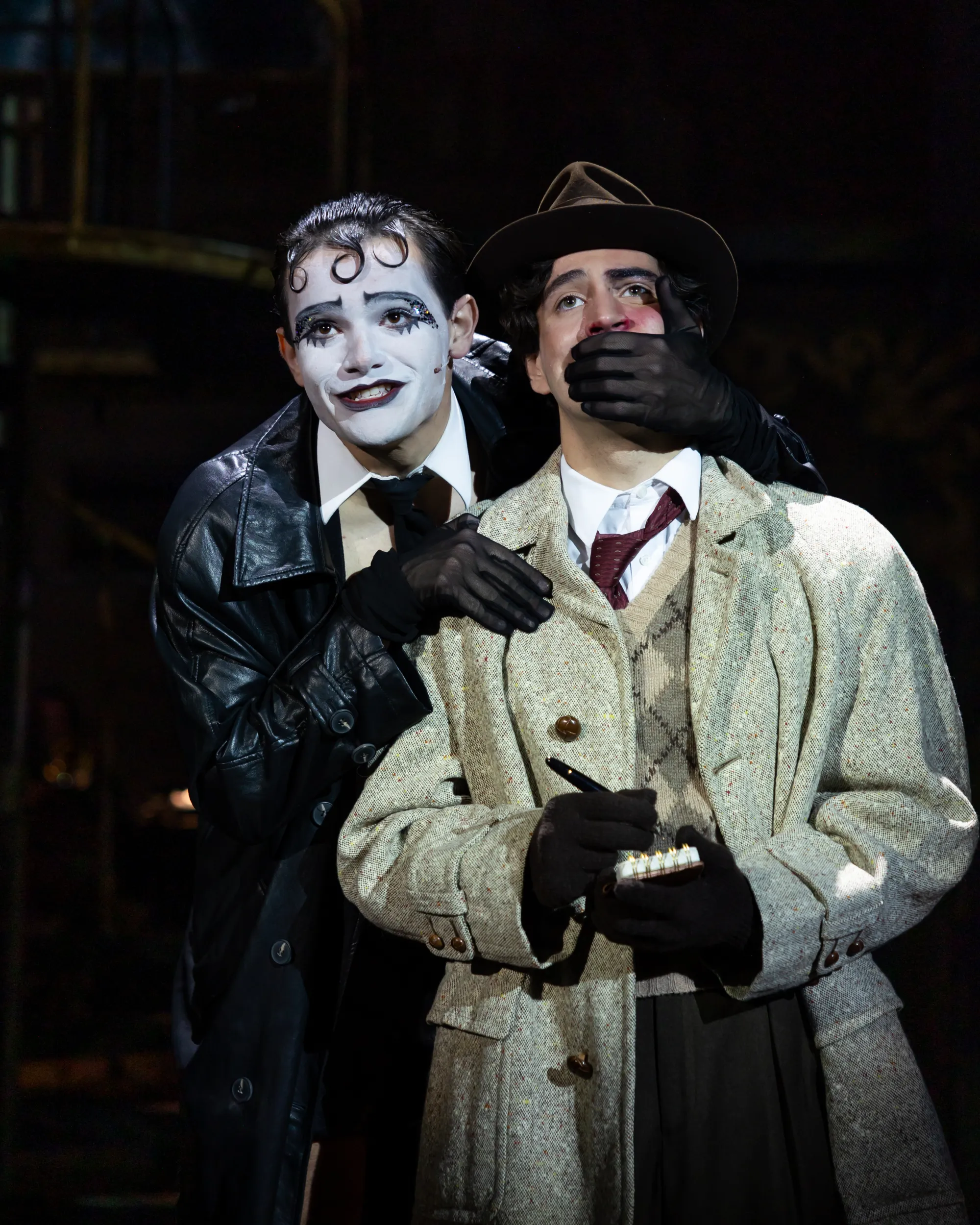 A man in white face paint holds his hand over another's mouth