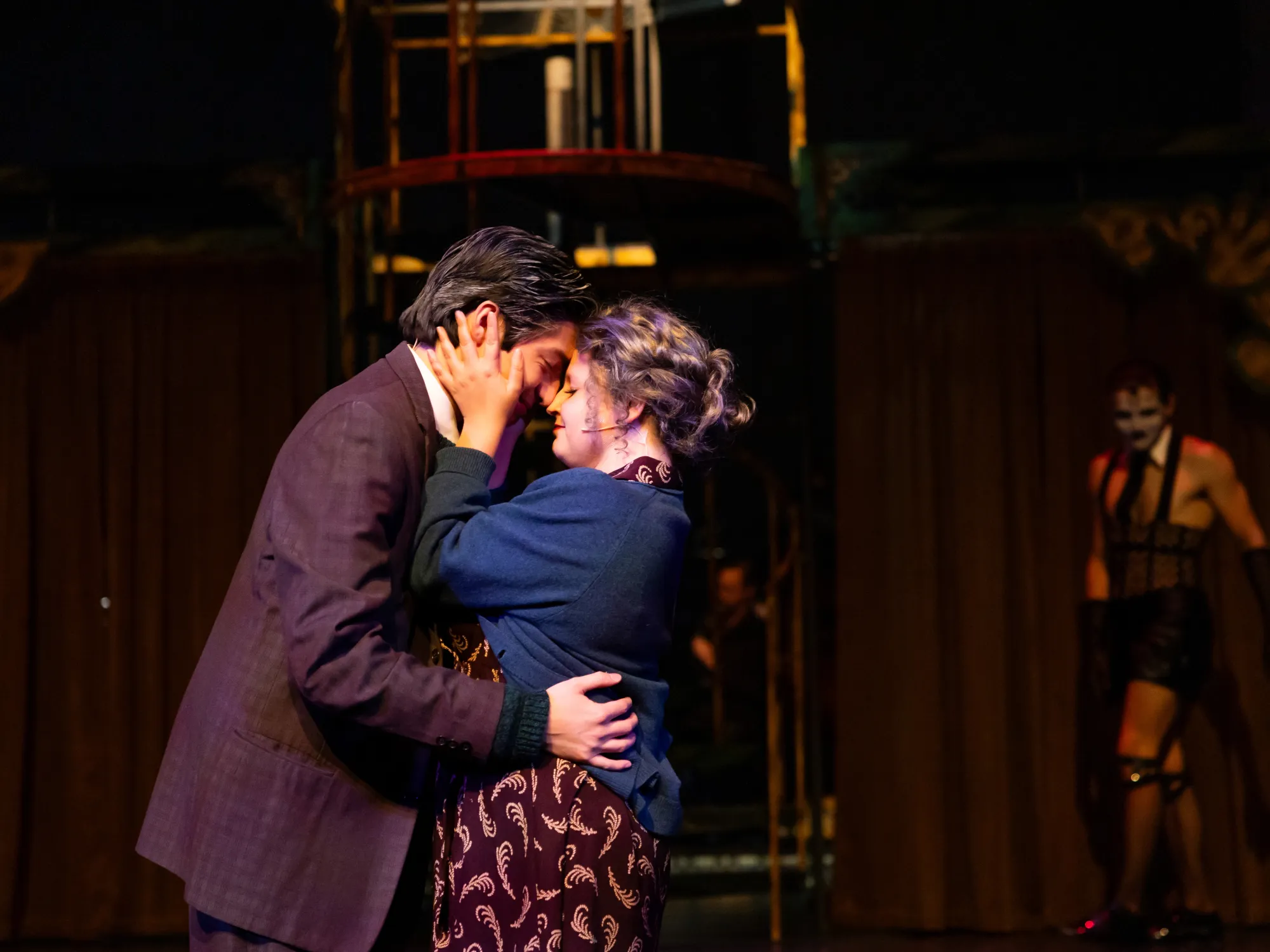 A couple touches forehead while a man watches in the background