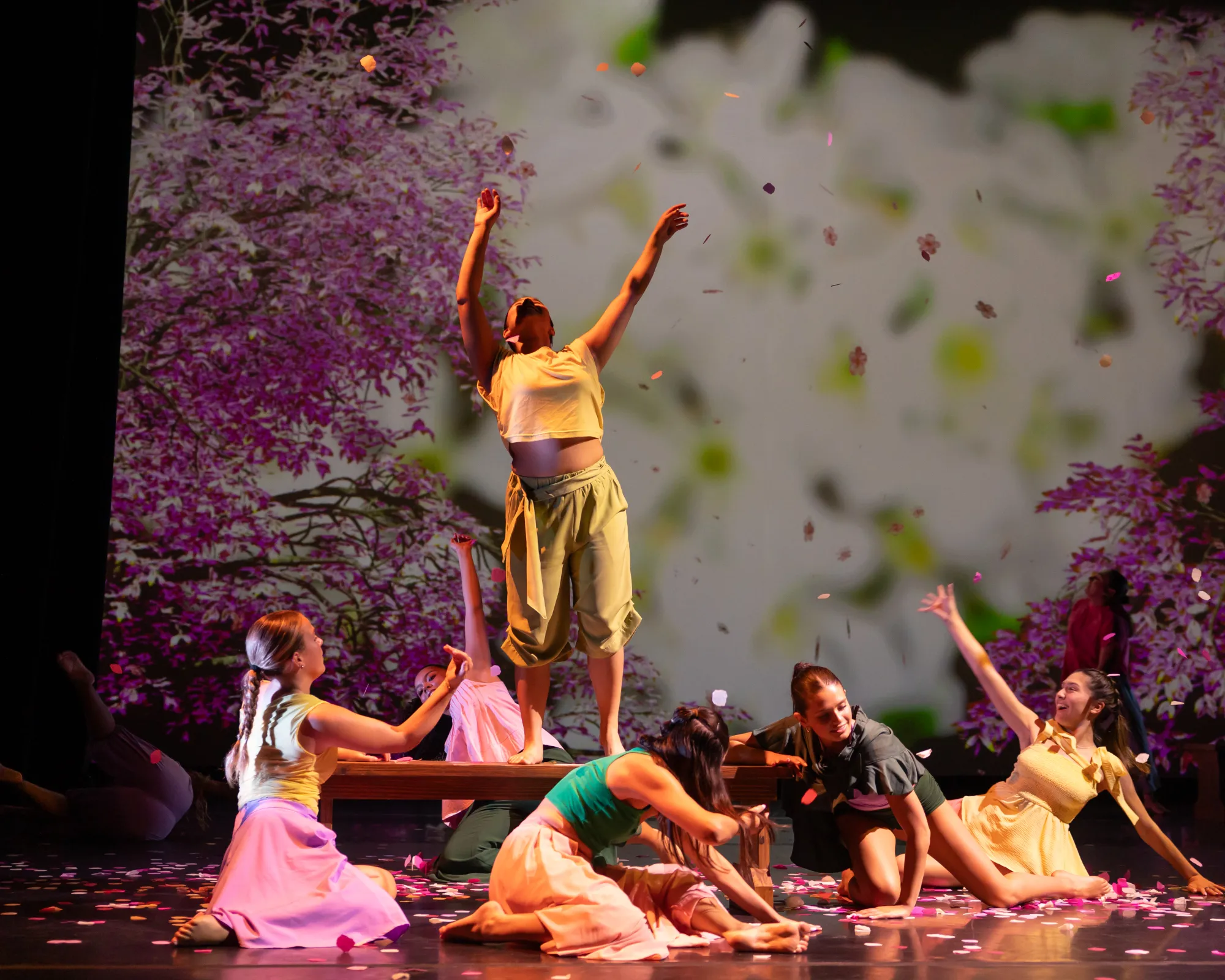 A dancer reaches upwards towards a blossoming cherry tree