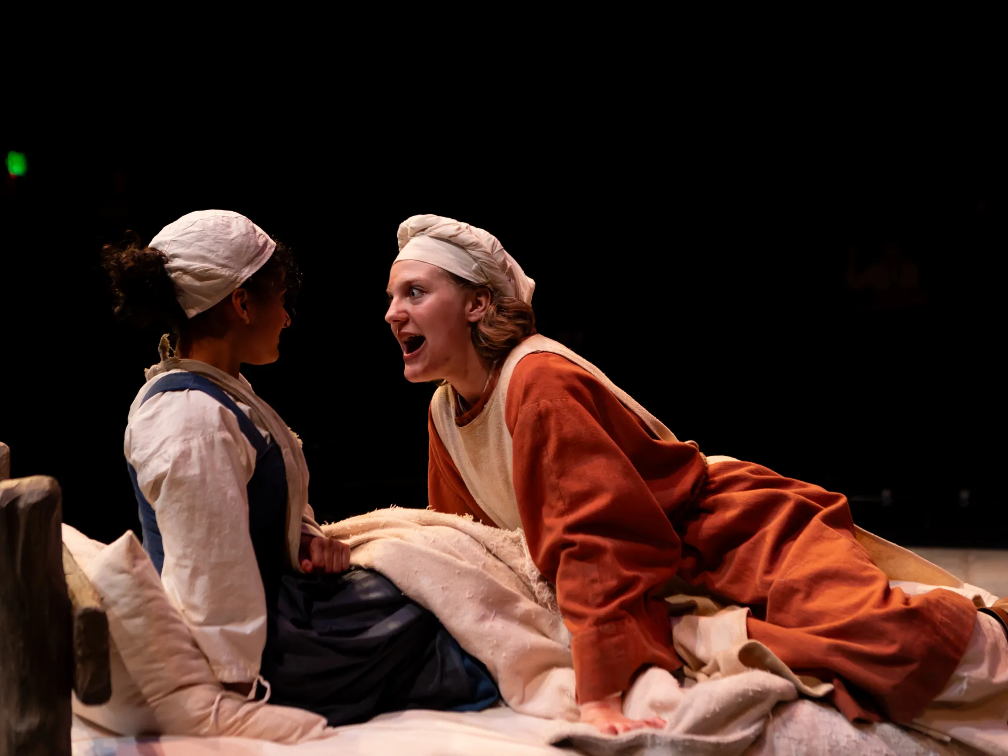 A girl on a bed leans over and smiles