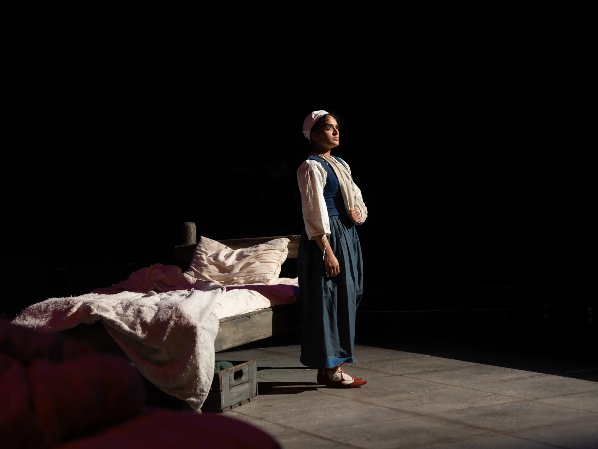 An actor in a blue dress stands facing a light