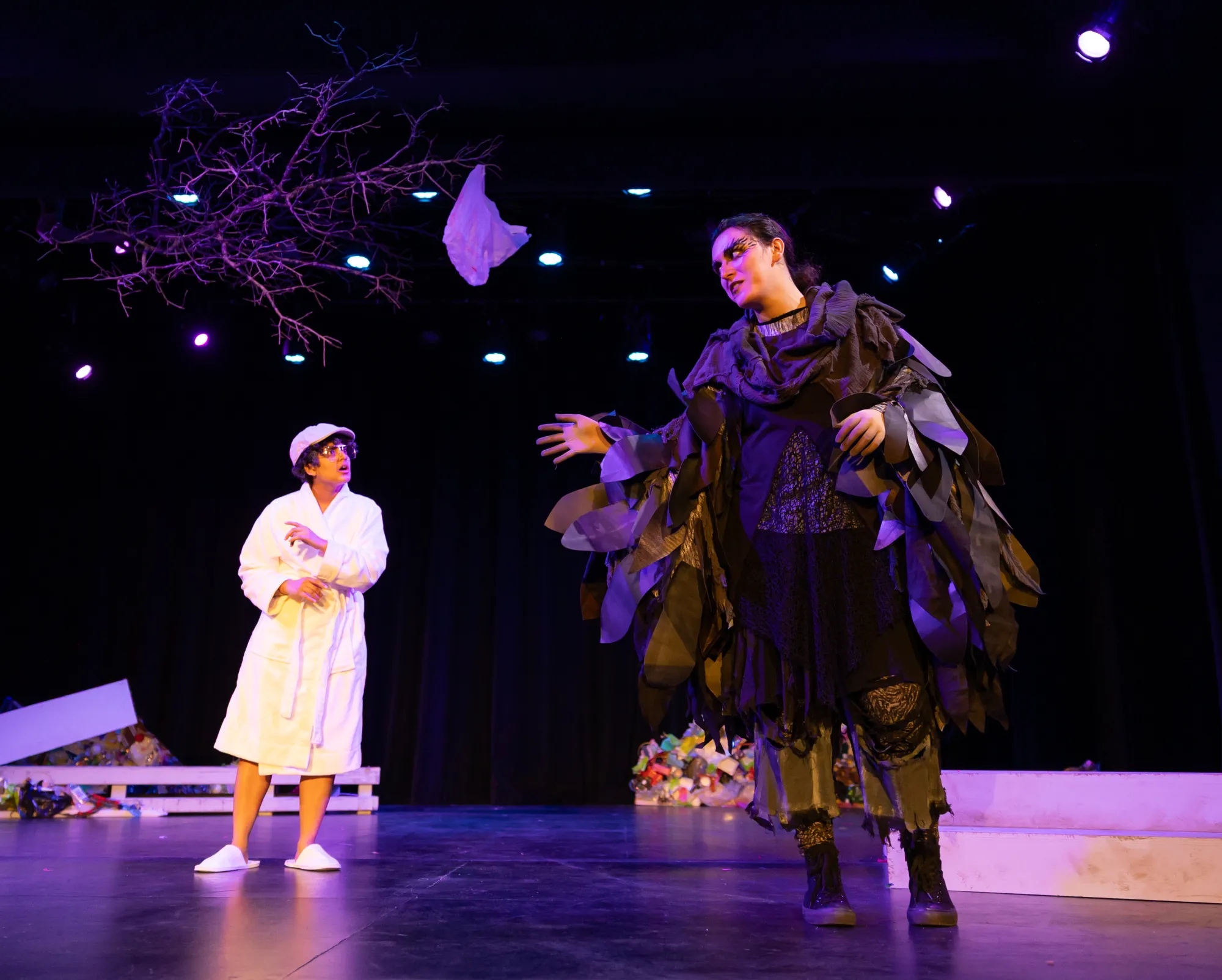 An actor in a robe looks towards another actor