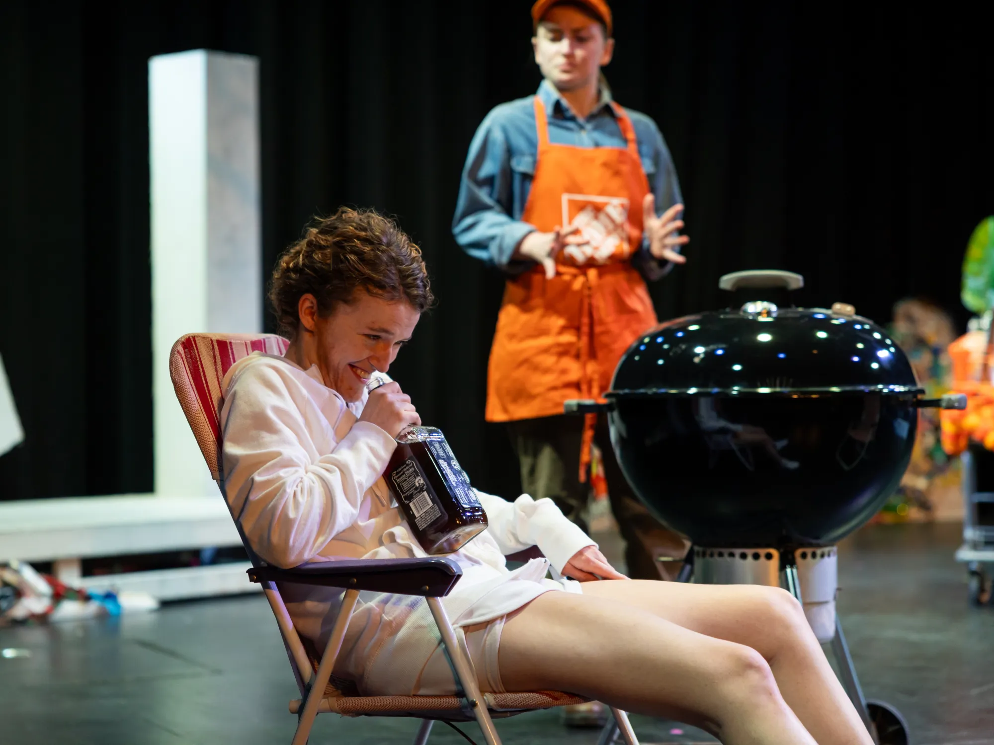 An actor dressed in white smiles into a bottle of whiskey