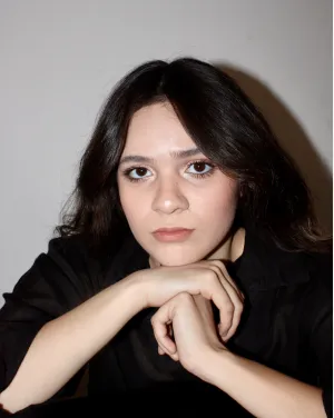 A woman with long black hair sets her head on her hands