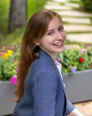 A woman in front of a bed of flowers turns around and smiles