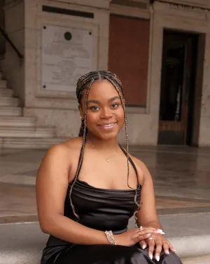A woman in a black satin dress with braids smiles