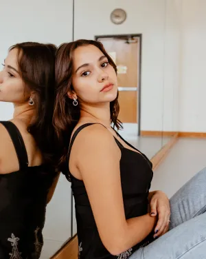 A woman sitting in front of a mirror turns toward the camera
