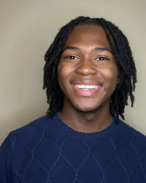 A person with locs wearing a blue sweater smiles