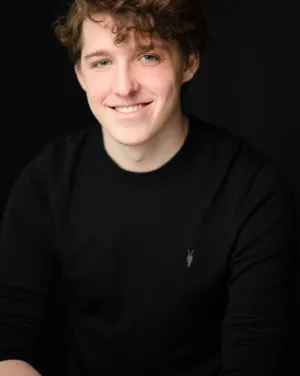 A man with brown hair in a black sweater smiles