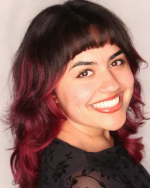 A woman with black hair with pink tips turns and smiles