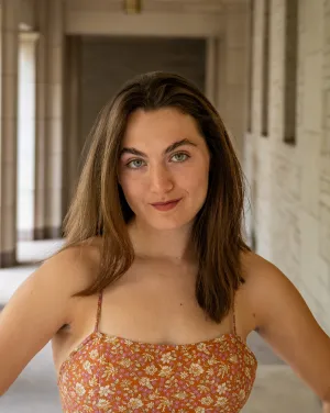 A woman with brown hair stands with her hands on her hips and smiles