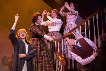 women on a staircase with bowing man at the bottom